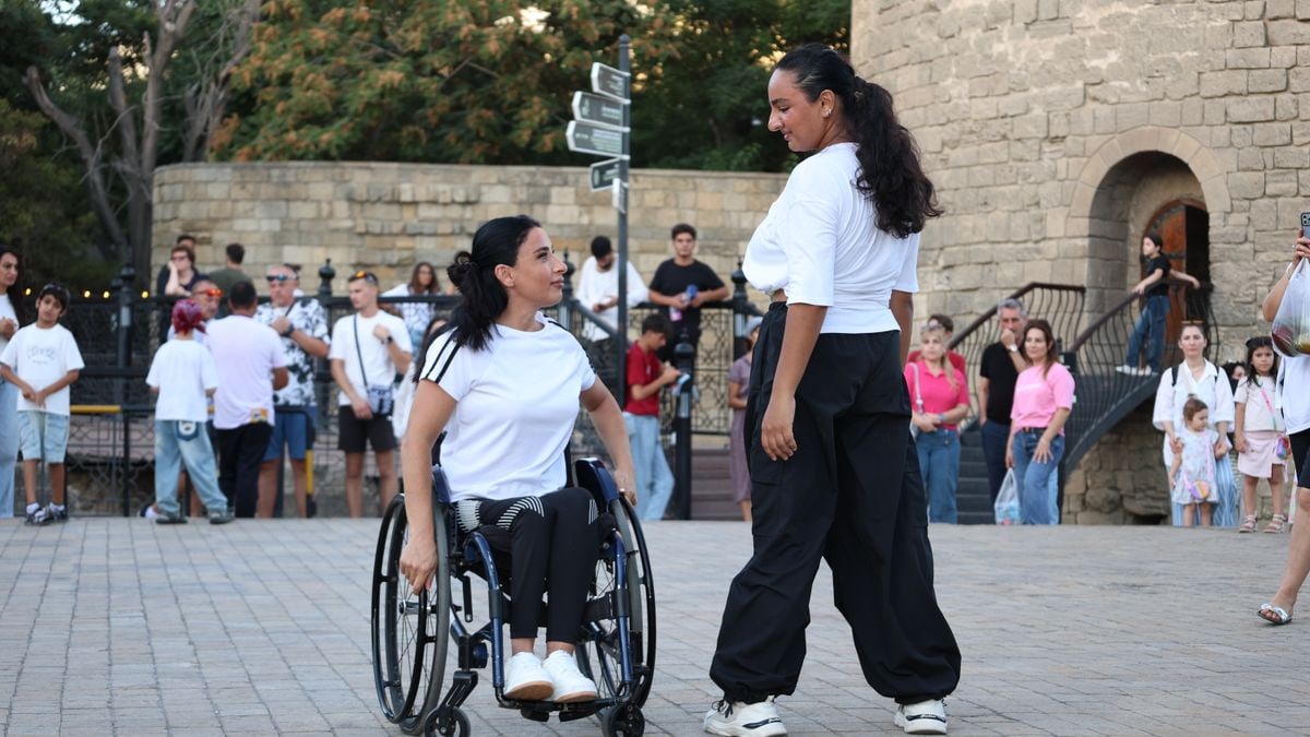 Two women, one in a wheelchair, performing a dance outdoors in front of an audience.