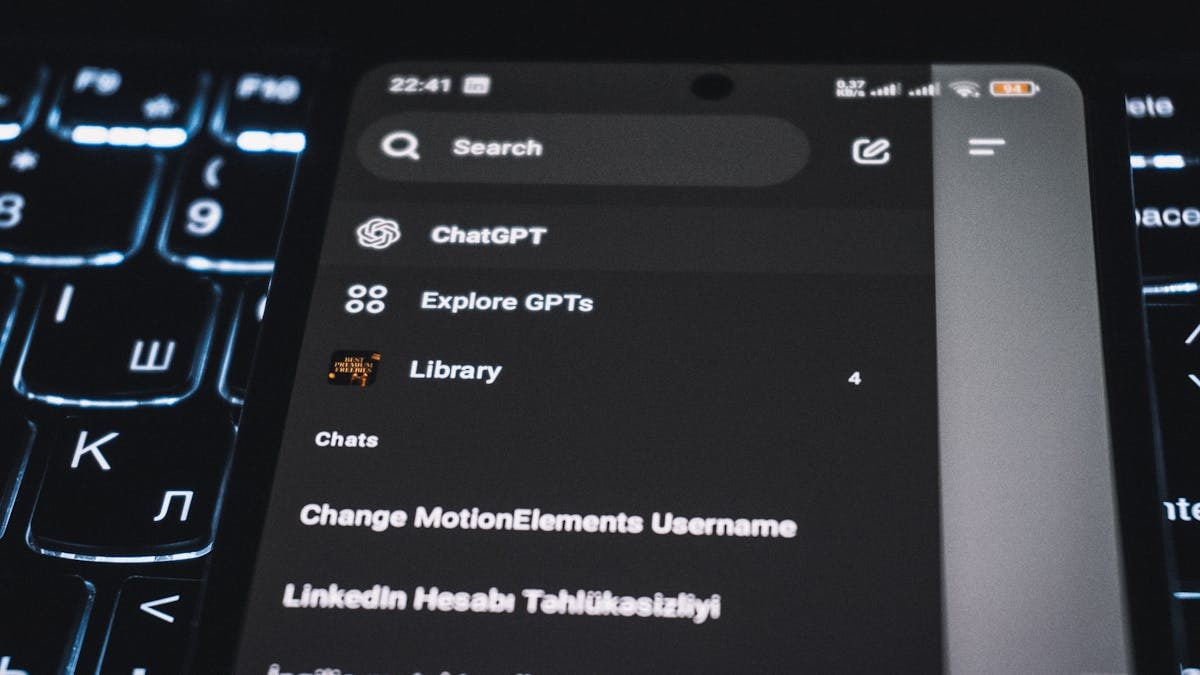 Close-up of a smartphone displaying a chat app interface with a backlit keyboard in the background.